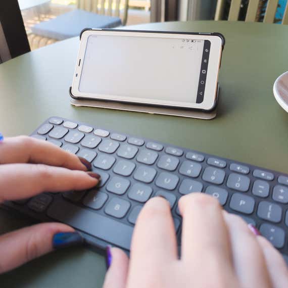 Two hands typing on a Logitech Keys-to-Go 2 keyboard in front of a Boox Palma 2 e-reader.